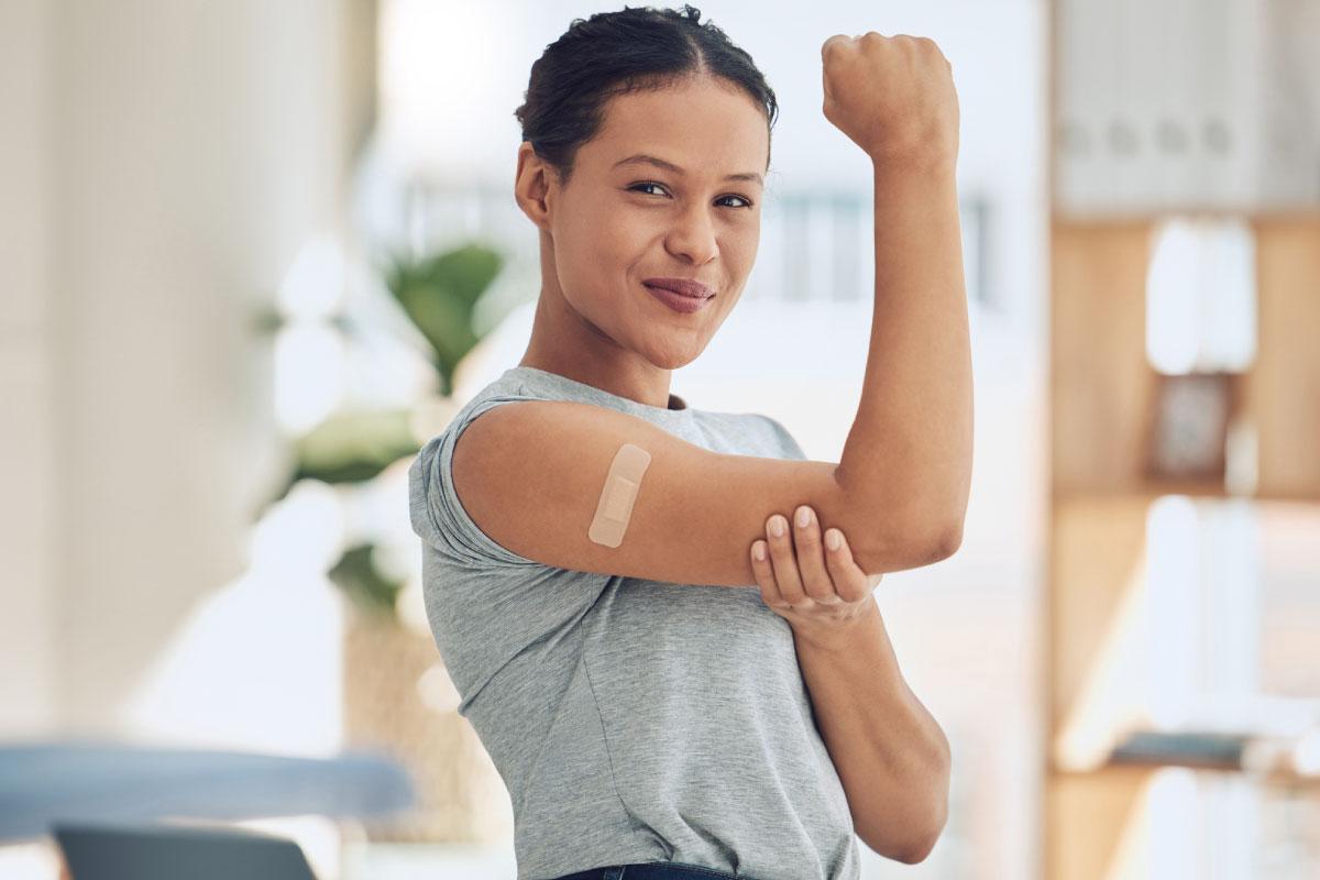 Women flexing her arm with a band aide from a shot.